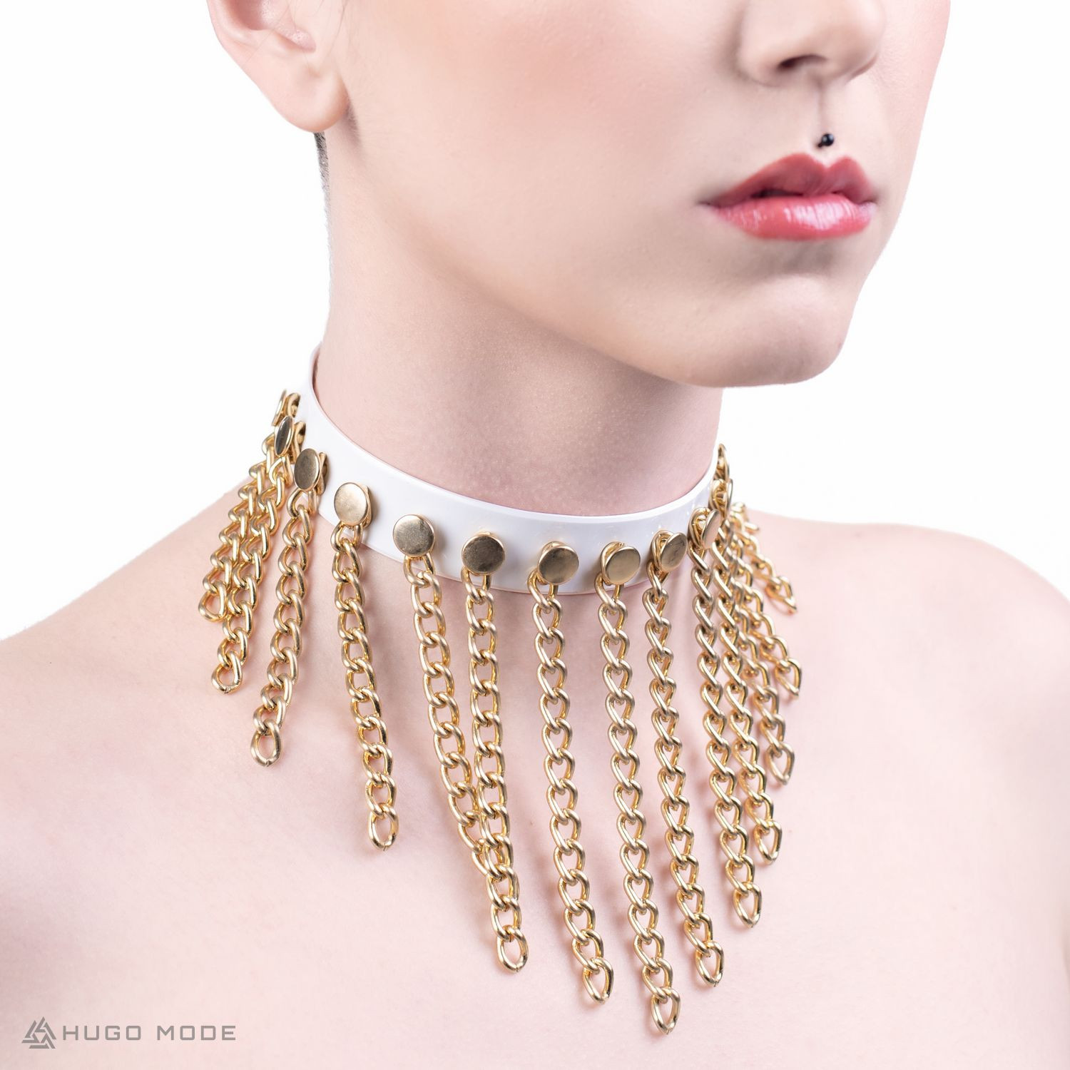 Ein weißes Choker Halsband verziert mit goldenen Ketten.